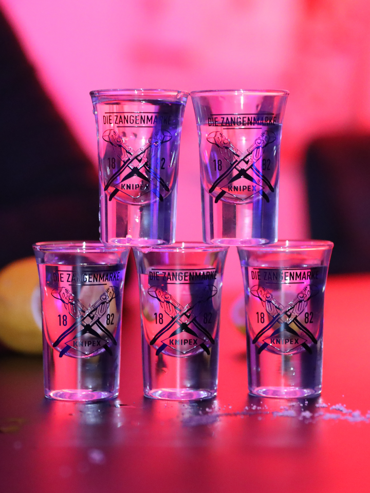 Fünf gestapelte Schnapsgläser mit Knipex-Logo und der Aufschrift 'Die Zangenmarke 1882', beleuchtet in pink.