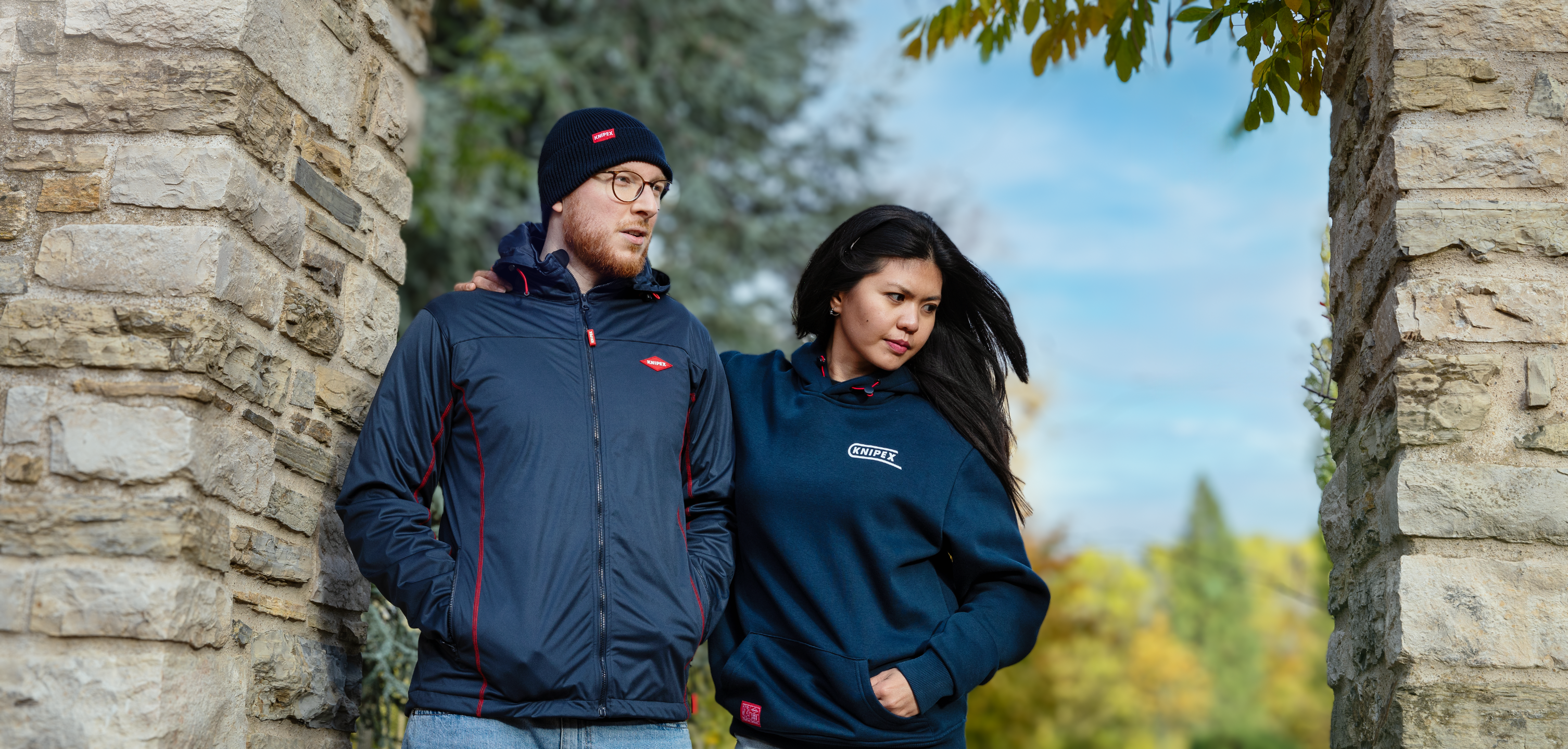 Zwei Personen tragen dunkelblaue Kleidung mit Knipex-Logo, eine Jacke und einen Hoodie, zwischen zwei Mauern 