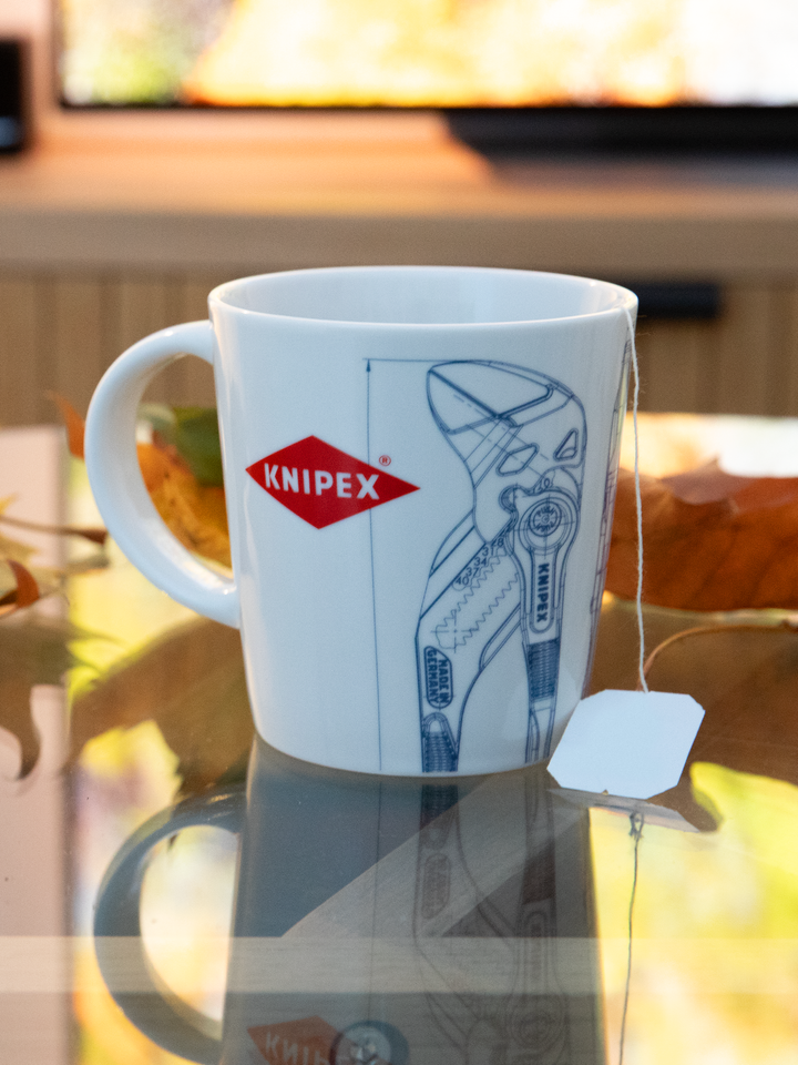 Weiße Tasse mit Knipex-Logo und einer technischen Zeichnung einer Wasserpumpenzange, mit Teebeutel darin 