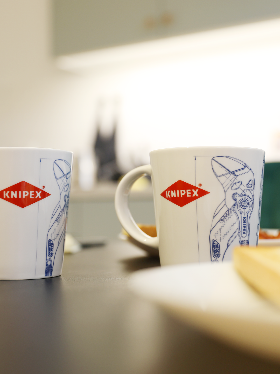 Weiße Tassen mit Knipex-Logo und einer technischen Zeichnung einer Wasserpumpenzange, vor unscharfem Hintergrund 